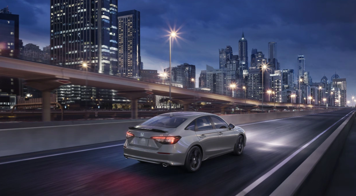 2026 Honda Civic grey driving on the highway at night with Montreal skyscrapers in the background.